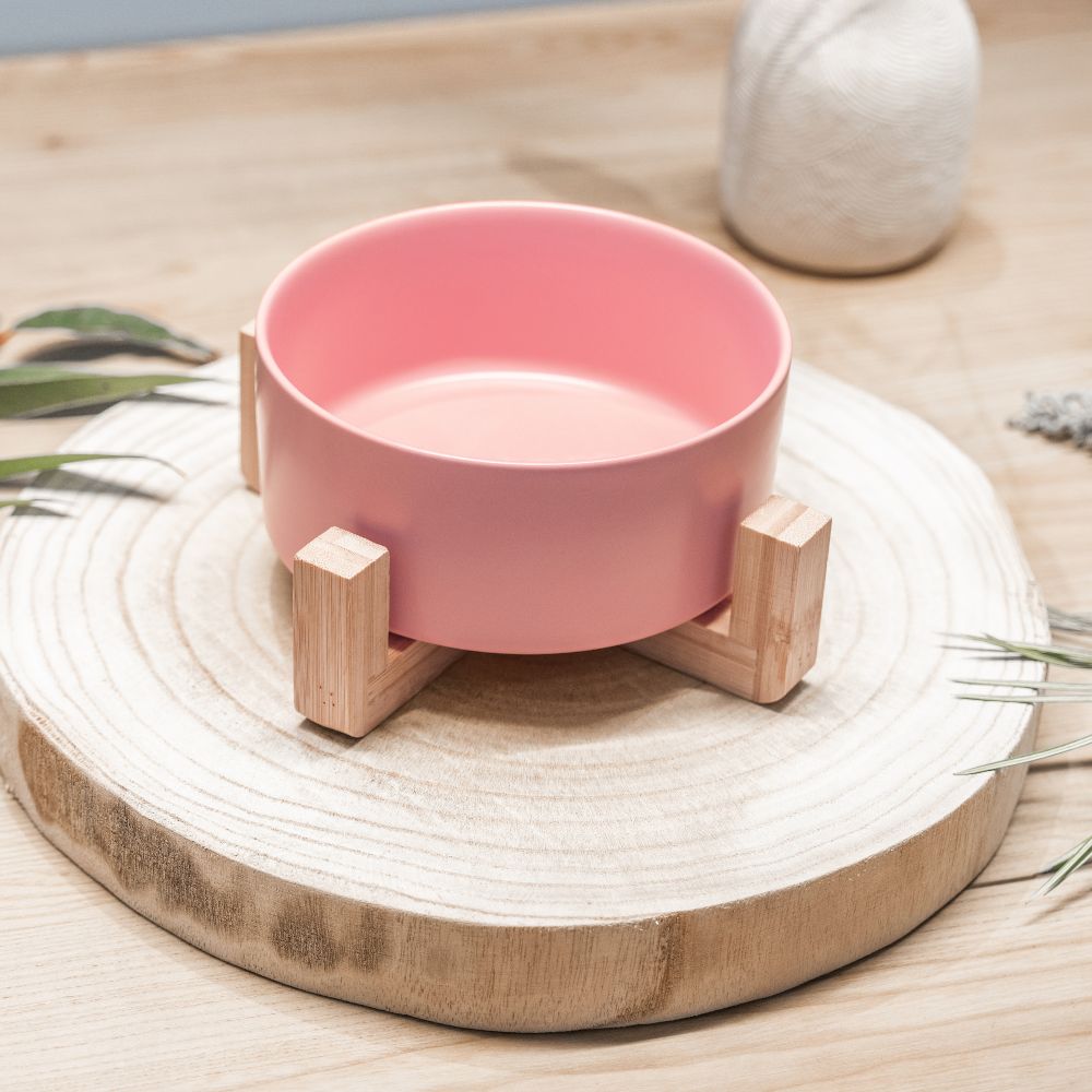 Petal pink ceramic pet bowl side view with eco-friendly bamboo stand on wooden board by Pet Store Collective. Dishwasher safe ceramic bowl, chip-resistant, and holds up to 850ml of pet food or water.