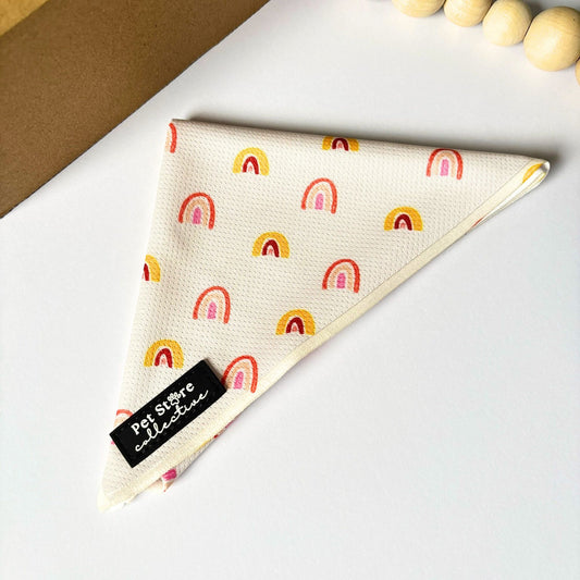 Front angled view of our Boho Rainbow Dog Bandana in soft golden yellow  rainbow print, shown flat on a white background with natural wooden bead styling. Lightweight polyester tie-on design by Pet Store Collective.