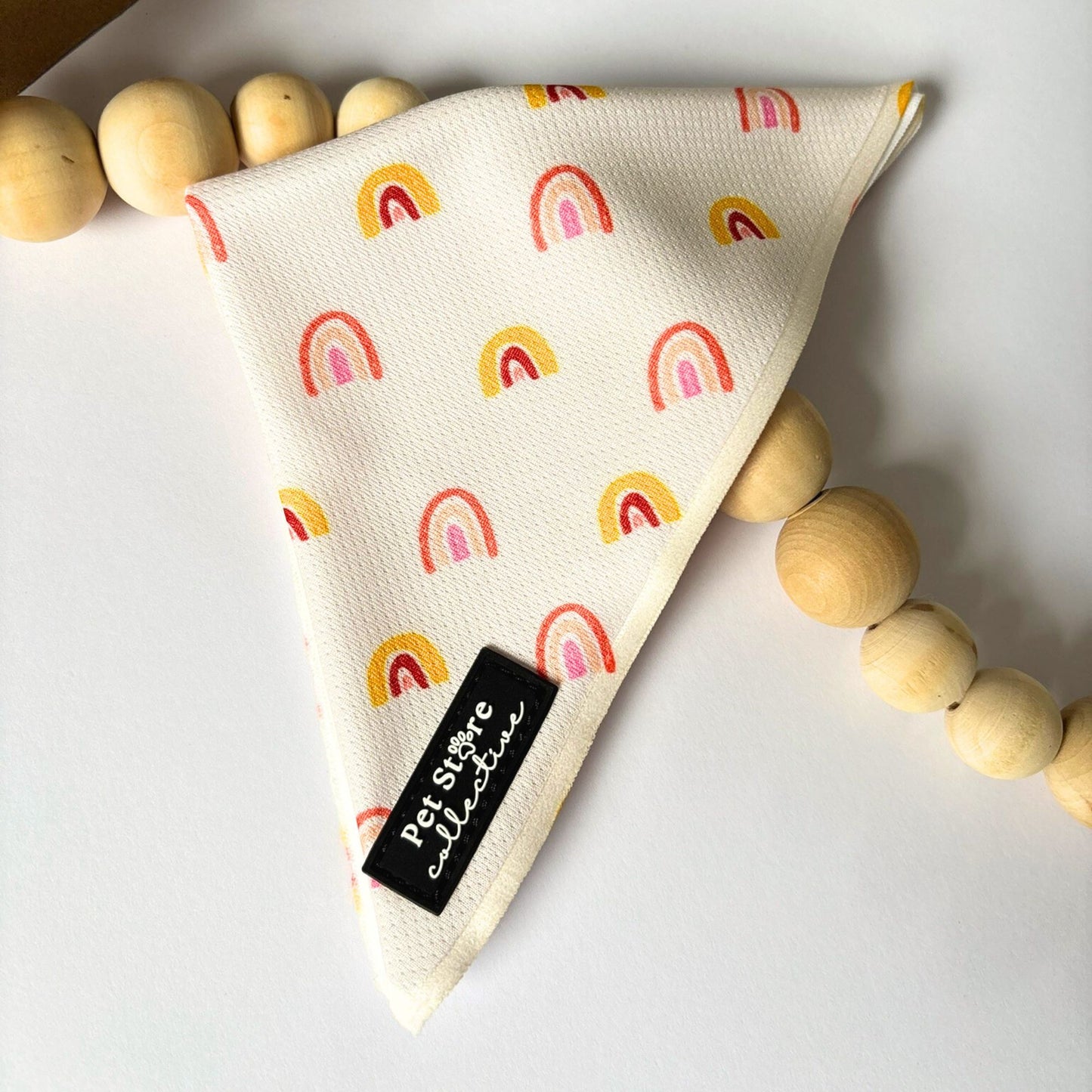 Close-up of our Boho Rainbow Dog Bandana featuring golden yellow and peach rainbow print on soft polyester fabric. Tie-on pet accessory for dogs and cats, available in two adjustable sizes.