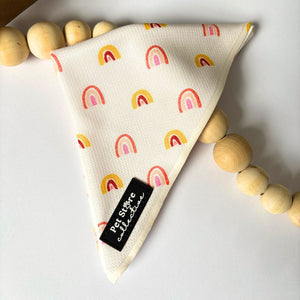 Close-up of our Boho Rainbow Dog Bandana featuring golden yellow and peach rainbow print on soft polyester fabric. Tie-on pet accessory for dogs and cats, available in two adjustable sizes.