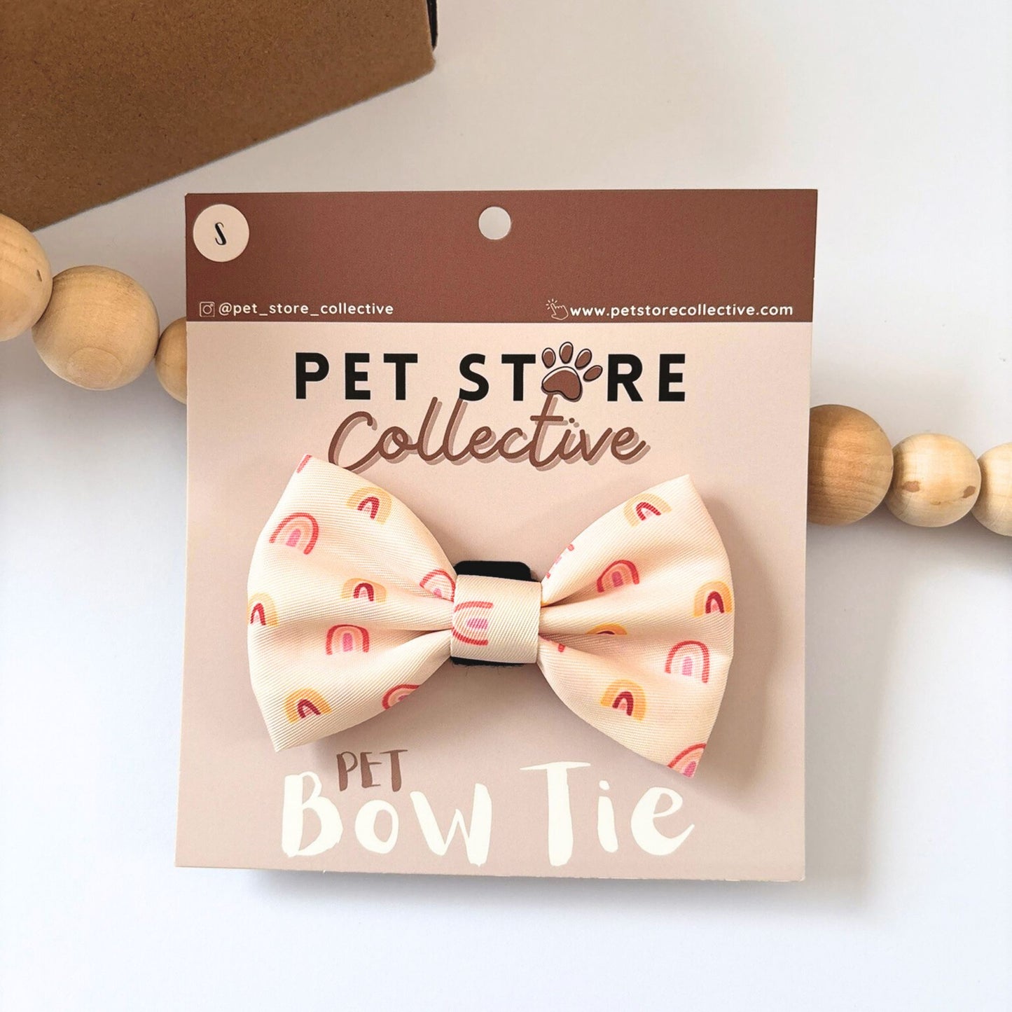 Pet Store Collective Boho Rainbow Dog Bow Tie attached to our custom packaging card, stylish golden rainbow design in soft peach and yellow tones. Made from durable polyester with velcro backing that fits securely on any collar for dogs and cats, available in small and large sizes.