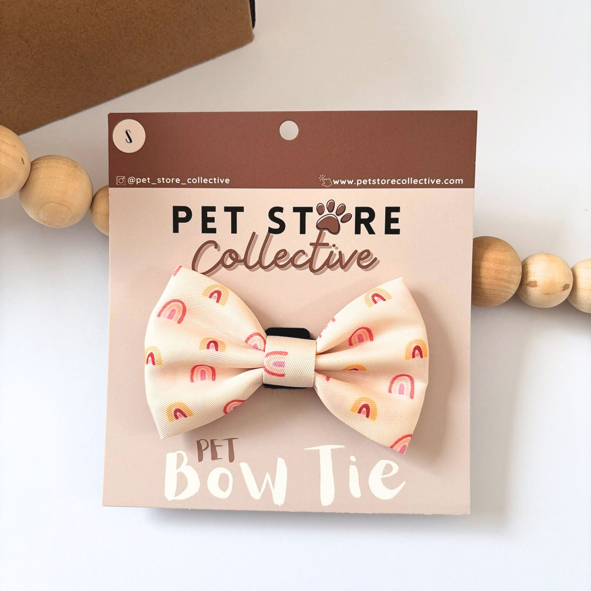 Pet Store Collective Boho Rainbow Dog Bow Tie attached to our custom packaging card, stylish golden rainbow design in soft peach and yellow tones. Made from durable polyester with velcro backing that fits securely on any collar for dogs and cats, available in small and large sizes.