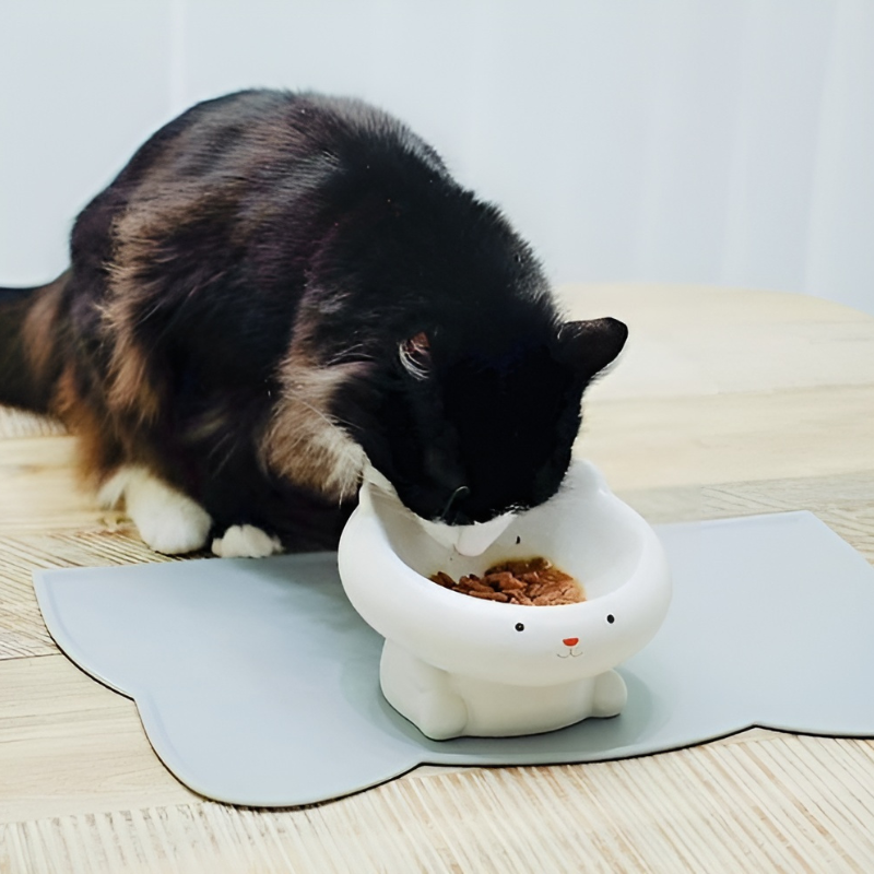 Black and white tuxedo cat enjoying a meal on the adorable ear-shaped waterproof silicone pet food mat, showcasing its practicality and charm.