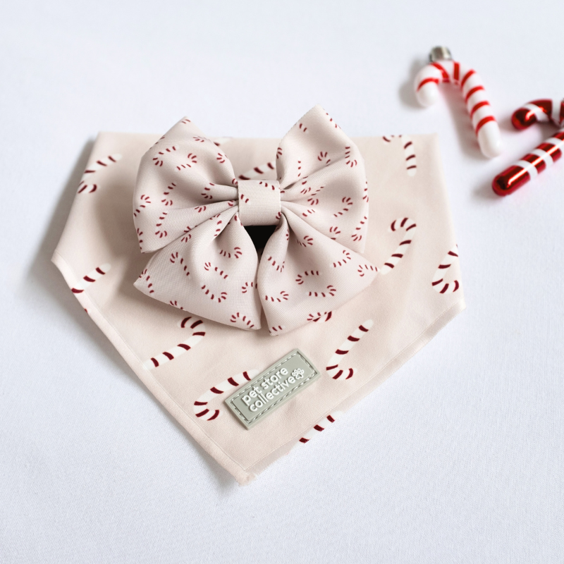 Festive Candy Cane Pet Bandana & Bow Tie Set, featuring red stripes on white candy canes. Bandana S/M (25-47cm neck), bow tie 9x6cm. Limited edition design from Pet Store Collective.