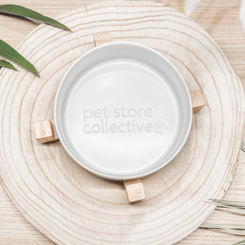 White Cloud Ceramic Pet Bowl with a bamboo base, measuring 19.5 cm in length and 9 cm in height. This durable bowl holds 3.6 cups (850 ml) and features high edges to minimise spills. Dishwasher-safe for easy cleaning, it has a crisp white finish with a natural bamboo base and an embossed Pet Store Collective logo inside the bottom of our ceramic bowl.