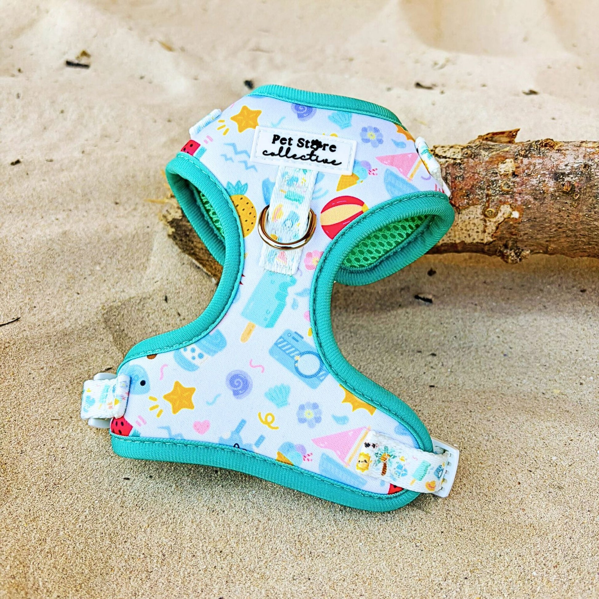 Our limited release Summer Bliss Adjustable Dog Harness front-facing on sand. Featuring a vibrant beachside print with palm trees, shells, and cheerful summer icons. Made from lightweight quick-dry neoprene with a breathable padded mesh interior and durable front D-ring for no-pull traning, designed by Pet Store Collective for stylish summer walks.