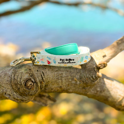 Our limited release Summer Bliss Dog Lead resting on a branch with ocean in the background. Featuring our exclusive beachside print, soft turquoise neoprene-padded handle, and strong yet lightweight design for everyday summer adventures.