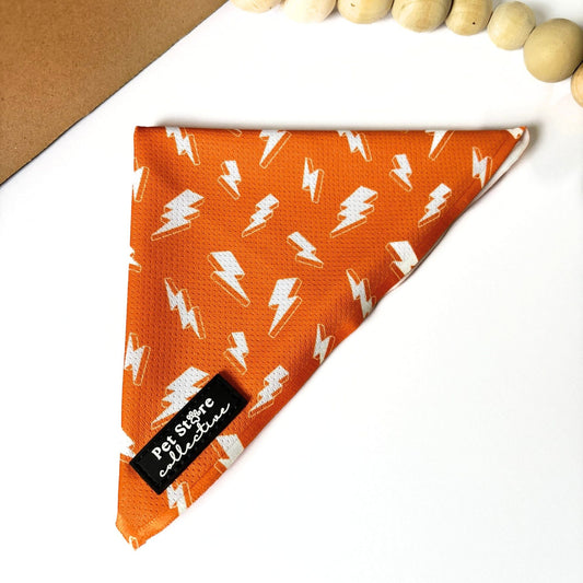 Front view of our Thunderbolt Dog Bandana in bright orange with white thunderbolts design. Shown flat with Pet Store Collective logo label, lightweight polyester fabric for dogs and cats.