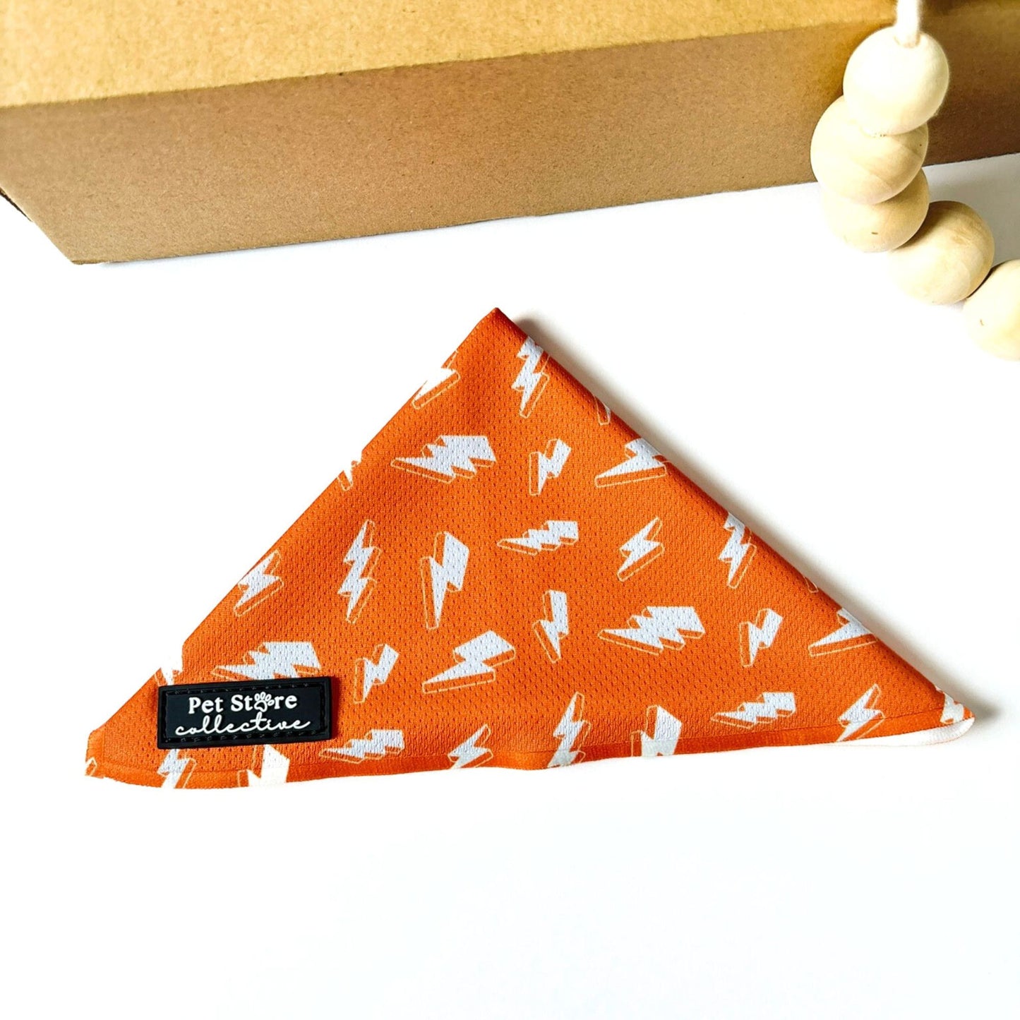 Straight front view of our Thunderbolt Dog Bandana in orange with bold white lightning bolt pattern. Pet Store Collective branding, lightweight polyester accessory for adventurous dogs and cats.