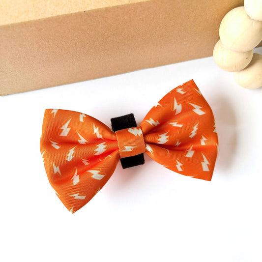 Large Thunderbolt Dog Bow Tie in bright orange with bold white thunderbolt pattern. Pet Store Collective logo, lightweight polyester with velcro backing for easy collar attachment for cats and dogs.