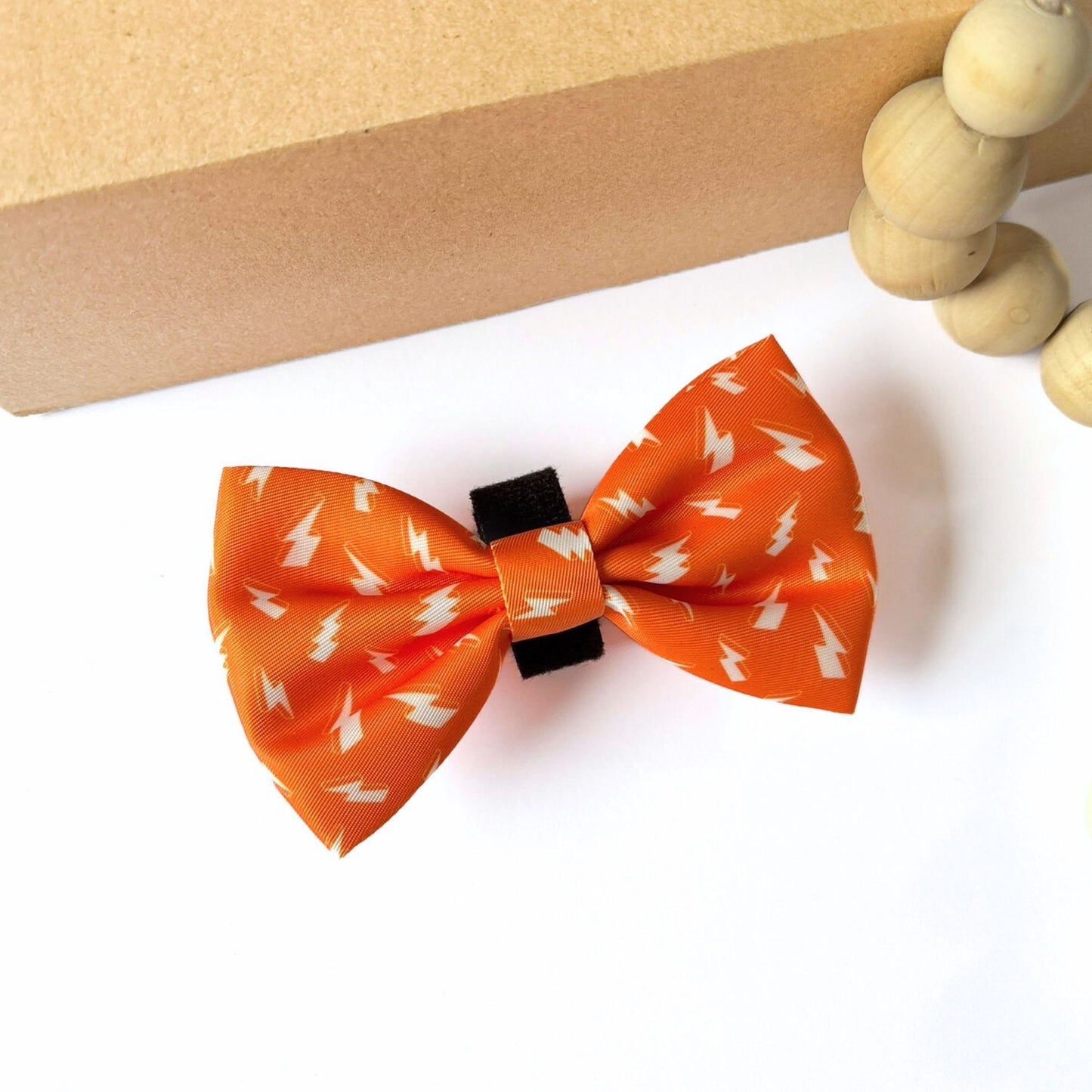 Angled view of Thunderbolt Dog Bow Tie in vibrant orange with white thunderbolts. Size Small (6cm height x 9cm width), made from soft lightweight polyester with velcro fastening to fit any pet collar.