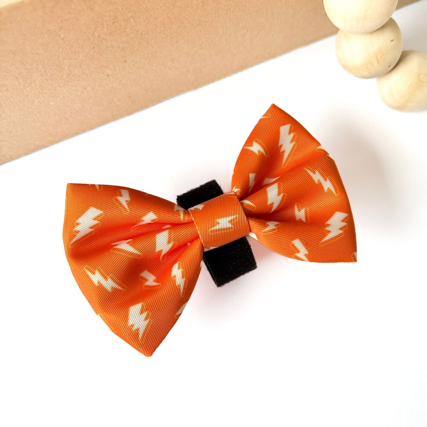 Angled side view Thunderbolt Dog Bow Tie in orange with striking white thunderbolts. Durable polyester bow tie accessory for cats and dogs, available in two sizes.