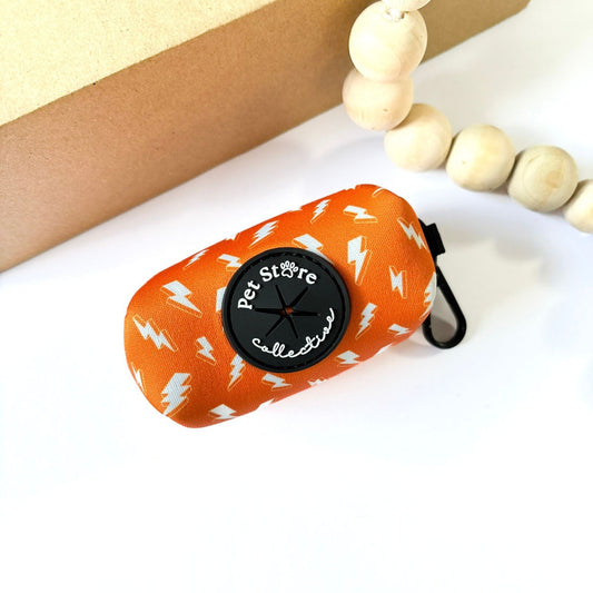 Thunderbolt Dog Poop Bag Holder in orange with white thunderbolts. Pet Store Collective logo label and rubber dispenser for quick bag access, made from durable neoprene.