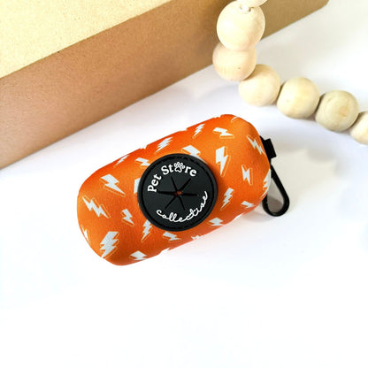 Thunderbolt Poop Bag Holder in orange with white thunderbolt pattern. Shown at an angle with Pet Store Collective rubber dispenser and clip for attaching to a lead, handbag, or belt to.