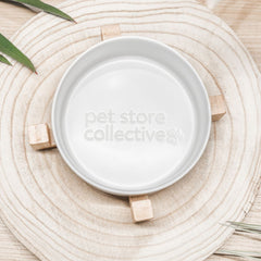 White ceramic pet bowl top view showing engraved Pet Store Collective logo with bamboo base on wooden board.